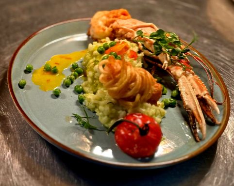 Ein Teller mit Garnelen, Risotto, Erbsen und einer gegrillten Tomate.