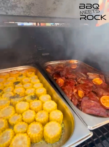 Grillplatte mit Maiskolben und mariniertem Fleisch, umgeben von Rauch.