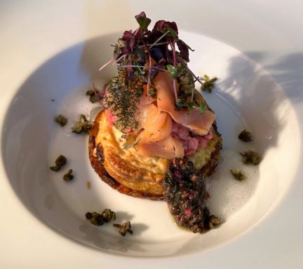 Gourmetgericht mit Fisch, Kräutern und buntem Salat auf einer weißen Platte.